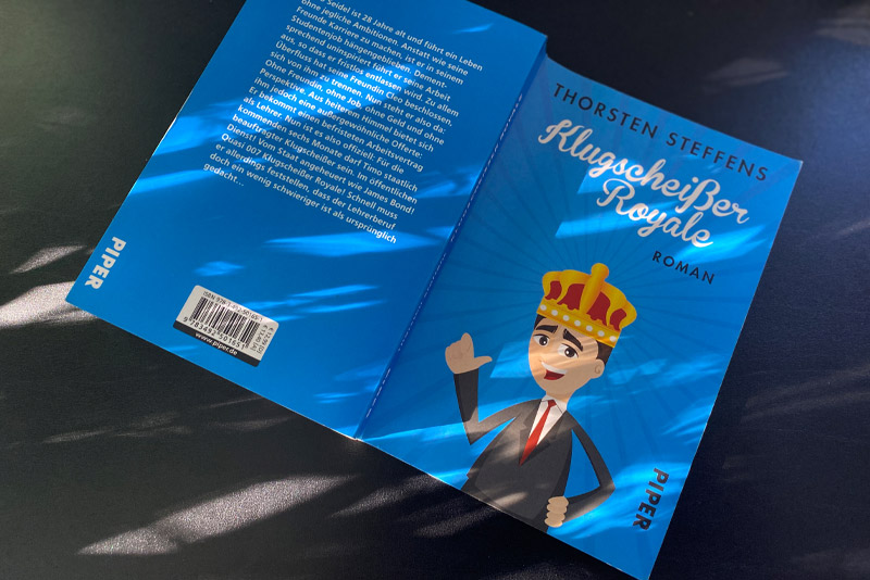Eine Taschenbuchausgabe von Klugscheißer Royale von Thorsten Steffens aufgeklappt